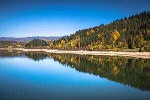 Autumn forest reflected in water. Colorful autumn morning in the mountains. Colourful autumn morning in mountain lake. Colorful autumn landscape photo