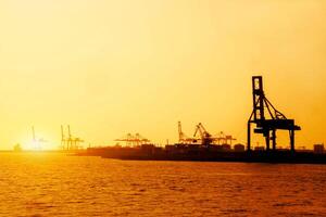 Silhouette of container and gantry crane at Osaka port are loading on evening with sunset glow background. photo