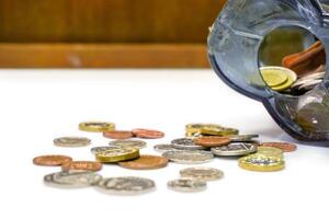 British currency coins open from the piggy bank laid out scattered on white table and wooden background. photo