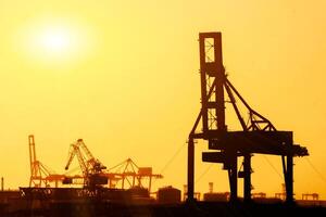 Closeup and Silhouette of container and gantry crane at Osaka port are loading on evening with sunset glow background. photo