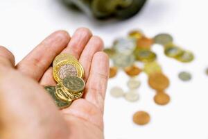 British currency coins on hand and blurry coins open from the piggy bank laid out scattered on white background. photo