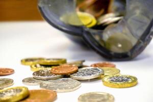 de cerca y cosecha de británico moneda monedas abierto desde el cerdito banco puesto fuera dispersado en blanco mesa y de madera antecedentes. foto