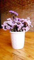 Purple flowers in a white ceramic vase on a wooden table photo