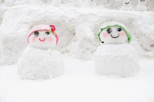 Boy and girl cute snowman kid wearing green and pink wool hat show for tourist snap photo in the Otaru Snow Light Path Festival at Otaru, Hokkaido prefecture, Japan