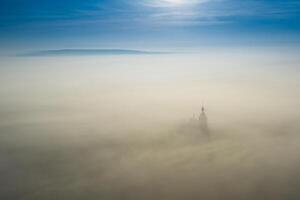 Surreal view of church almost completely hidden by fog photo