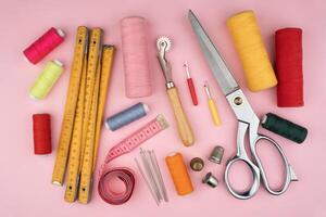 various tailor accessories and tools for tailoring on a pink background photo