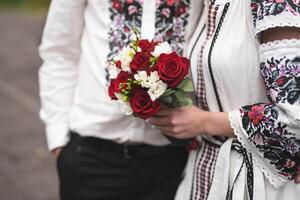 the bride and groom are holding hands with a bouquet of flowers and in traditional Ukrainian clothes photo