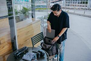 joven indonesio hombre preparando o embalaje fotografía equipo y ropa dentro un mochila. fiesta viaje concepto. foto