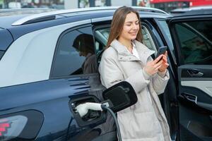 Young woman charging her electric car at a charging station in the city. Eco fuel concept. The concept of environmentally friendly transport. Recharging battery from charging station. photo