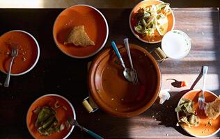 Top view of empty clay dish tagine and dirty plates with the rest of food after dinner on a wooden table photo