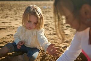 de cerca retrato de caucásico hermosa pequeño muchachas jugando con arena en el playa foto