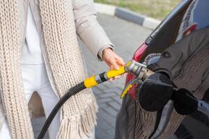 joven mujer repostaje coche con gasolina a gas estación. eco combustible concepto. el concepto de ambientalmente simpático transporte. foto