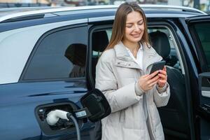 joven mujer cargando su eléctrico coche a un cargando estación en el ciudad. eco combustible concepto. el concepto de ambientalmente simpático transporte. recarga batería desde cargando estación. foto