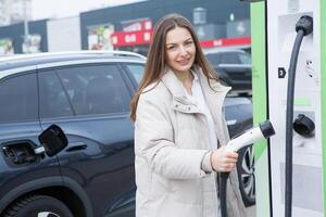 Young woman charging her electric car at a charging station in the city. Eco fuel concept. The concept of environmentally friendly transport. Recharging battery from charging station. photo