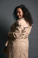 Beautiful curly haired gravid woman smiles looking at camera through her shoulder, isolated over fashion gray background photo