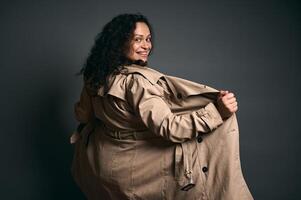 Cheerful curly haired expectant mother woman smiles looking at camera through her shoulder, isolated gray background photo