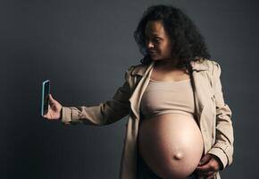 Attractive beautiful young gravid female, expectant mother photographing her tummy in third trimester of happy pregnancy photo