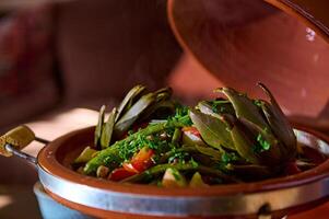 alcachofas y verduras sazonado con Cortado cilantro y perejil hierbas, servido en tradicional marroquí tagine arcilla plato foto