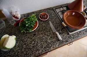 todavía vida parte superior ver Roca mostrador y un plato con cilantro y perejil, Cortado verduras, maduro Olivos, tagine arcilla foto