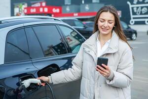 Young woman charging her electric car at a charging station in the city. Eco fuel concept. The concept of environmentally friendly transport. Recharging battery from charging station. photo