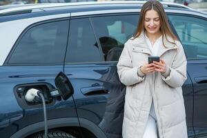 Young woman charging her electric car at a charging station in the city. Eco fuel concept. The concept of environmentally friendly transport. Recharging battery from charging station. photo