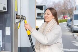 joven mujer repostaje coche con gasolina a gas estación. eco combustible concepto. el concepto de ambientalmente simpático transporte. foto