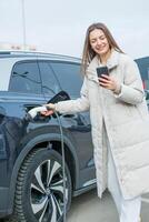 Young woman charging her electric car at a charging station in the city. Eco fuel concept. The concept of environmentally friendly transport. Recharging battery from charging station. photo