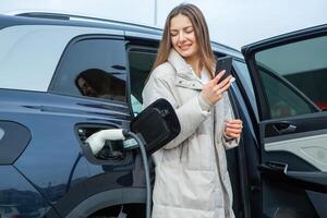 Young woman charging her electric car at a charging station in the city. Eco fuel concept. The concept of environmentally friendly transport. Recharging battery from charging station. photo