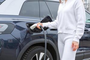 Young woman charging her electric car at a charging station in the city. Eco fuel concept. The concept of environmentally friendly transport. Recharging battery from charging station. photo