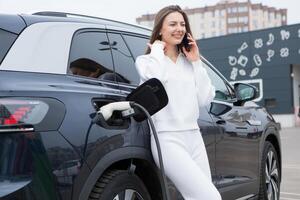 joven mujer cargando su eléctrico coche a un cargando estación en el ciudad. eco combustible concepto. el concepto de ambientalmente simpático transporte. recarga batería desde cargando estación. foto