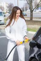 joven mujer repostaje coche con gasolina a gas estación. eco combustible concepto. el concepto de ambientalmente simpático transporte. foto