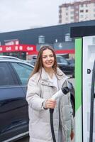 Young woman charging her electric car at a charging station in the city. Eco fuel concept. The concept of environmentally friendly transport. Recharging battery from charging station. photo