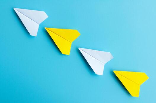 parte superior ver de blanco y amarillo papel aviones origami volador en azul antecedentes. foto