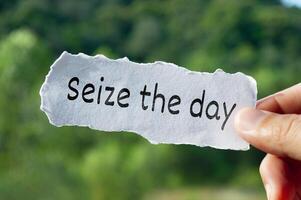 Seize the day text on torn paper with hand holding on nature background photo