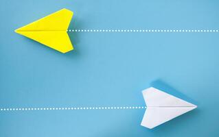 Top view of yellow and white paper airplane origami flying to a different direction on blue background photo