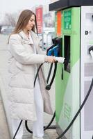 Young woman charging her electric car at a charging station in the city. Eco fuel concept. The concept of environmentally friendly transport. Recharging battery from charging station. photo