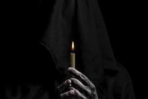 Young catholic nun is holding candle in her hands. Focus on candle. Face is blurred. Photo on black background.