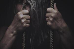 sad young girl holding a steel cage in old iron bar. children prison and prisoner concept photo