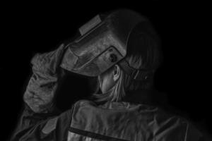 Welder man in the helmet and with welding terminals in the hand on the black wall background with copy space shows a thumbs up gesture. photo