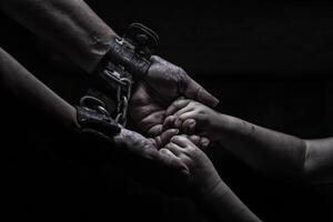 a woman in shackles holds a child by the hand on a black background photo