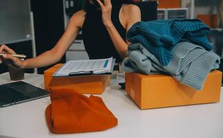 Fashion blogger concept, Young Asian women selling clothes on video streaming.Startup small business SME, using smartphone or tablet taking receive and checking in home office photo