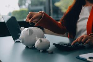 A young girl works at a laptop, writes a business development plan in a notebook, develops a strategy and makes calculations of earned funds. A woman puts her savings in a piggy bank. photo