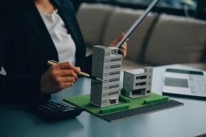 Close up realtor sit at table holds tiny house model, layout of cottage. Real estate purchase, new property, ownership, construction company make special offer to client, affordable dwelling concept photo