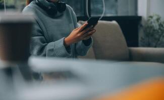 Happy pretty millennial Indian girl relaxing at home, resting in armchair, typing on smartphone, using online app, software, shopping on Internet, making video call. Mobile phone communication photo