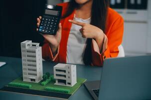 Close up realtor sit at table holds tiny house model, layout of cottage. Real estate purchase, new property, ownership, construction company make special offer to client, affordable dwelling concept photo