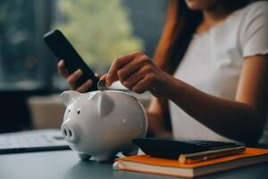 Young Asian woman saving for retirement Saving money through a piggy bank and taking notes on notebook, savings concept. photo