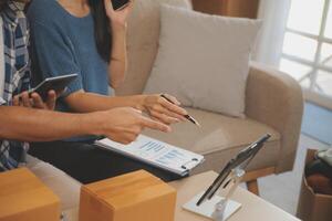Two Asian blogger showing clothes in front of the camera to recording vlog video live streaming at her shop. Online Shopping Cart notion. on sofa at home photo
