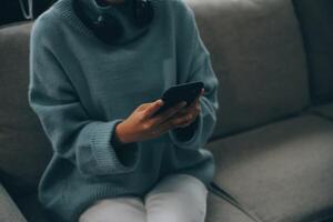 Happy pretty millennial Indian girl relaxing at home, resting in armchair, typing on smartphone, using online app, software, shopping on Internet, making video call. Mobile phone communication photo