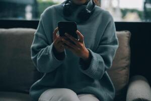 Happy pretty millennial Indian girl relaxing at home, resting in armchair, typing on smartphone, using online app, software, shopping on Internet, making video call. Mobile phone communication photo