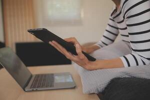 Young attractive asian woman resting using browsing tablet computer on sofa at home, happy girl sitting on couch relax reading digital gadget with excited, communication and lifestyle concept. photo